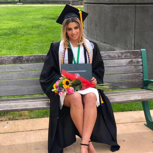 Carla Diab sitting on bench in a university wearing graduation cap and holding degree in black gaon